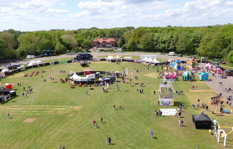 Luchtfoto van een buitenevenement met tenten, springkussens en wandelende mensen in een groene omgeving.